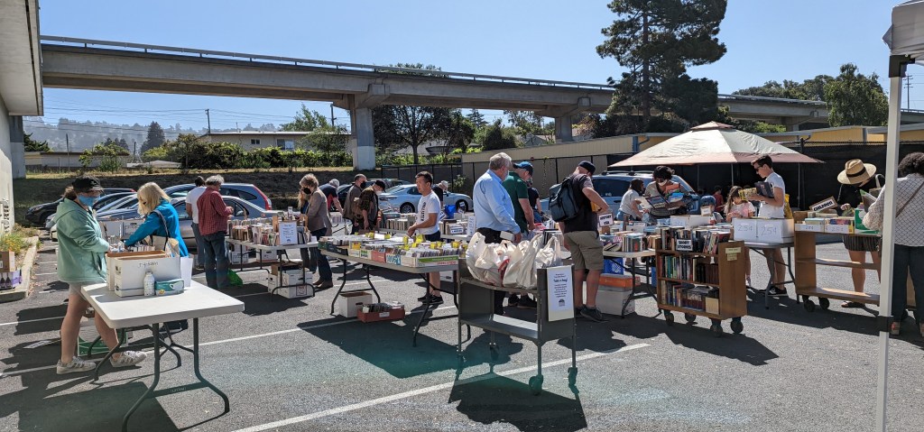 Friends book sale outside in the parking lot, with people looking at books on tables. May 2022
